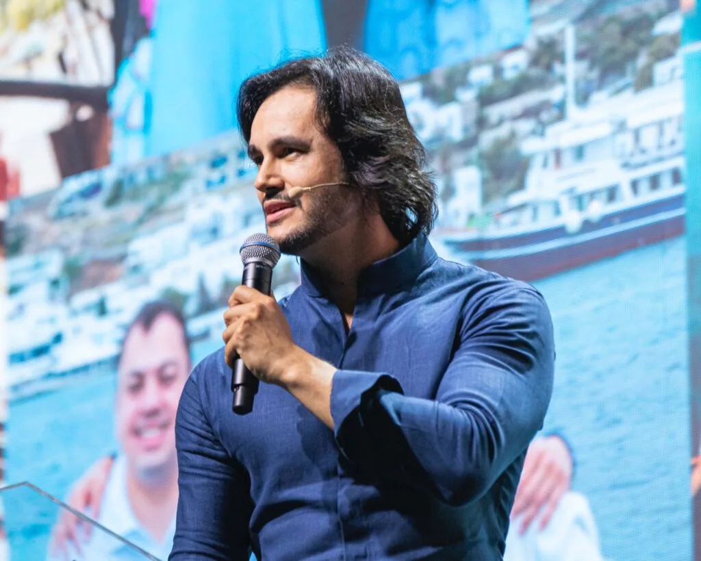 Pyero Tavolazzi no palco em evento empresarial com catamarã ao fundo